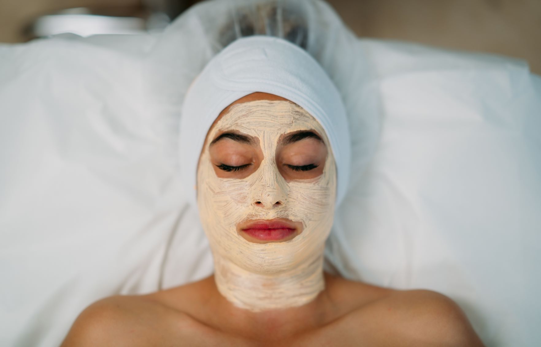 Client laying down with their eyes closed while receiving a facial treatment mask.