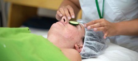 Skin care professional performing a facial on a client with cucumbers on their eyes.