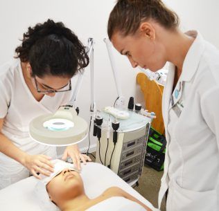 Esthetics instructor observing a student perform a skin care treatment on a client.