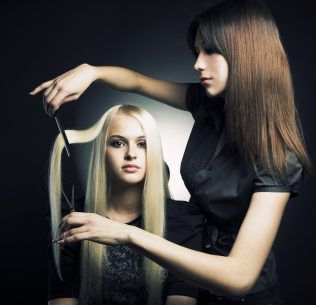 Woman holding scissors up to another woman's hair extensions.