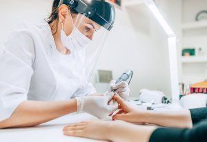 Nail Technician wearing a face mask and shield while giving a client a manicure