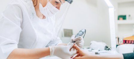 Nail Technician wearing a face mask and shield while giving a client a manicure