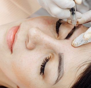 Permanent makeup, tattooing of eyebrows. Cosmetologist in white gloves applying make up with machine for woman in beauty salon