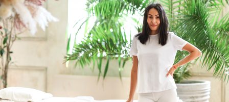 Woman skin care professional wearing white standing infront of a spa bed and lush plants.